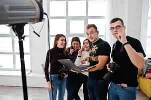 fotógrafo explicando sobre la toma a su equipo en el estudio y mirando en la computadora portátil. hablando con sus asistentes sosteniendo una cámara durante una sesión de fotos. trabajo en equipo y lluvia de ideas. foto