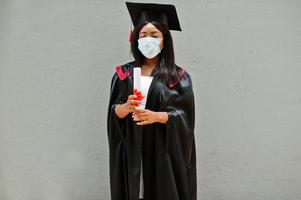 una joven estudiante graduada afroamericana usa una máscara protectora contra el coronavirus. concepto de ceremonia de graduación, cuarentena. foto