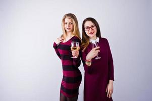 Two attractive friends in purple dresses drink sparkling wine or champagne in the studio. photo