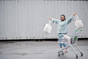 no más plástico. mujer africana con carrito de compras y bolsas ecológicas posadas en el mercado al aire libre. foto