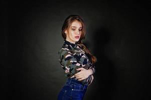 Handsome brunette girl wear military shirt and jeans, posing at studio against gray background. Studio model portrait. photo