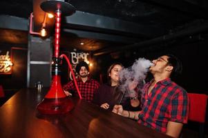 Group of indian friends sitting at lounge bar, smoke hookah and having rest. photo