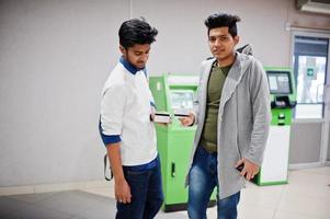 dos chicos asiáticos con tarjetas de crédito en la mano contra el cajero automático verde. foto