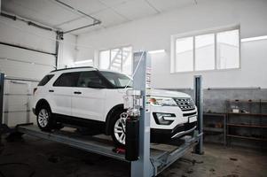 coche todoterreno americano en soporte para verificación de inclinación de alineación de ruedas en el taller de la estación de servicio. foto