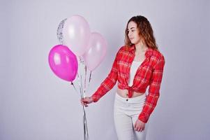 Young girl in red checked shirt and white pants with balloons against white background on studio. photo