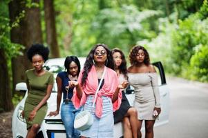 Group of five happy african american girls posed against car, one of them show keys. photo