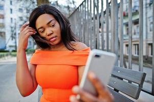 African american woman model xxl in orange dress looking on mobile phone. photo