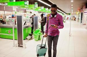 African american man in checkered shirt with suitcase and backpack. Black man against cashier supermarket. photo