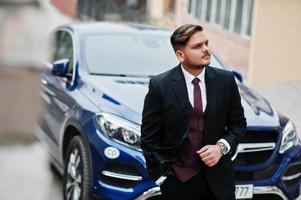Rich indian businessman in formal wear standing against business suv car. photo