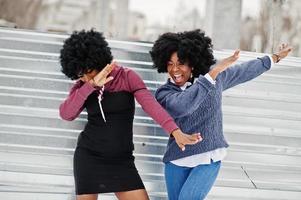 dos mujeres afroamericanas de pelo rizado usan suéteres posados en el día de invierno, haciendo dab. foto
