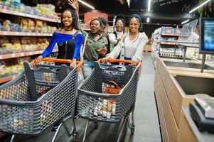 Group of five african womans walking and having fun together in supermarket with shopping carts. photo