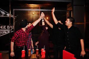 Group of indian friends having fun and rest at night club, drinking cocktails and giving high five together. photo
