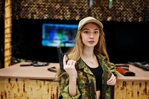 Military girl in camouflage uniform with gun at hand against army background on shooting range. photo