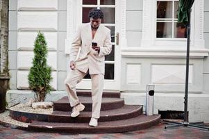 Stylish afro man in beige old school suit with mobile phone. Fashionable young African male in casual jacket on bare torso. photo