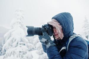 Man tourist photographer with backpack, at mountain with pine trees covered by snow. Beautiful winter landscapes. Frost nature. photo