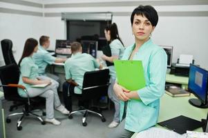 tema médico. retrato de una doctora con portapapeles contra un grupo de médicos reunidos en la oficina de resonancia magnética en el centro de diagnóstico del hospital. foto