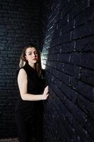 Portrait of a beautiful brunette girl in black jumpsuit in the studio next to the brick wall. photo
