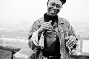 African american man in jeans jacket, beret and eyeglasses posed on abandoned roof. photo