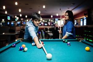 Stylish asian couple wear on jeans playing pool billiard on bar. photo