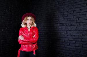 retrato de estudio de una chica rubia con sombrero rojo y chaqueta de cuero contra la pared de ladrillo. foto