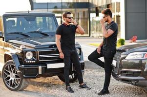 Two asian brothers man wear on all black posed near suv cars. photo