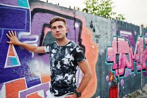 Lifestyle portrait of handsome man posing on the street of city with graffiti wall. photo