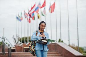 African student female posed with backpack and school items on yard of university, against flags of different countries. photo