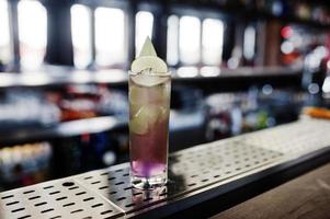 Alcoholic long violet cocktail with ice in glass at bar table. photo