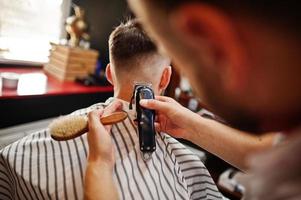 Young bearded man getting haircut by hairdresser while sitting in chair at barbershop. Barber soul. photo