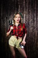 Young funny housewife in checkered shirt and yellow shorts pin up style with saucepan on wooden background. photo