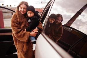 la joven madre y el niño se paran cerca de su auto todoterreno. concepto de conducción segura. foto