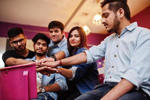 Group of stylish asian friends wear on jeans sitting at chairs against bar in club put hands on hands. photo