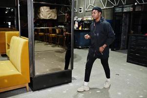 Handsome african american man posing  inside night club in black hat. photo