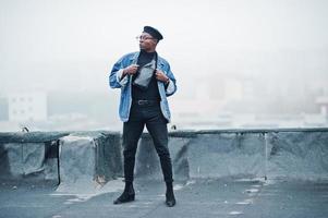 African american man in jeans jacket, beret and eyeglasses posed on abandoned roof. photo
