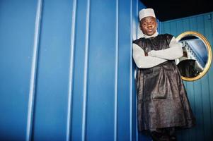 African men in black traditional clothes with cap against mirror on blue wall. photo