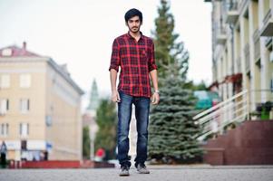 joven estudiante indio con camisa a cuadros roja y jeans posó en la ciudad. foto