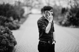 hombre indio con camisa marrón posó al aire libre y hablando por teléfono móvil. foto