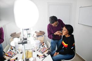 African American woman applying make-up by make-up artist at beauty saloon. photo