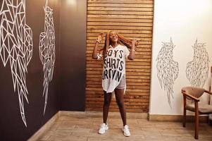 Beautiful african woman in stylish casual clothes posing against angel wings wall. She moving her hair dreadlocks. photo