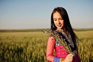 tierna niña india en sari, con maquillaje de labios violetas posada en el campo al atardecer. modelo indio de moda. foto