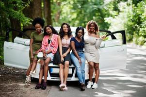 Group of five happy african american girls sitting on a car hood. photo