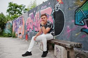 Lifestyle portrait of handsome man posing on the street of city with graffiti wall. photo