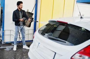 South asian man or indian male washing his white transportation on car wash. photo