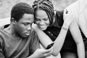 Couple of african american friends chill and sitting on poufs outdoor and look on phone. photo