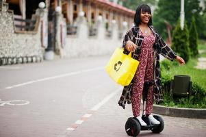 hermosa mujer afroamericana usando segway o hoverboard. chica negra con símbolo de reciclaje de bolsas ecológicas de tela amarilla. foto