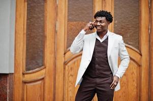 Thoughtful young handsome african american gentleman in formalwear. Black stylish model man in white jacket speak on phone. photo