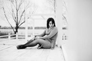 Portrait of brunette girl in gray dress sitting at white wooden construction. photo