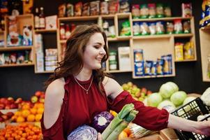 Girl in red holding different vegetables on fruits store. photo