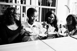 cuatro chicas afroamericanas sentadas en la mesa en el café y comiendo postre helado. foto
