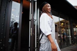 African american woman in overalls and beret walking out the door in outdoor terrace with christmas decorations. photo